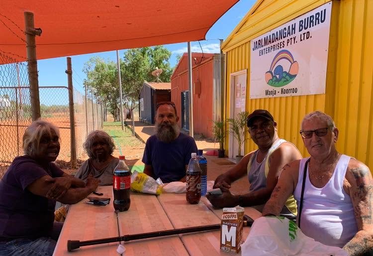 Community members at an outdoor table beside the yellow Jarlmadangah Burru Enterprises building