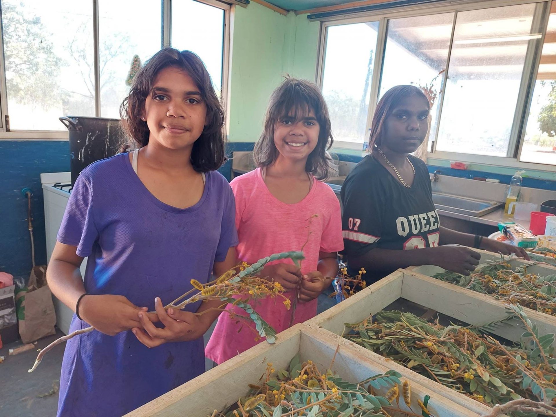 Three young people sorting freshly picked plants at a workbench