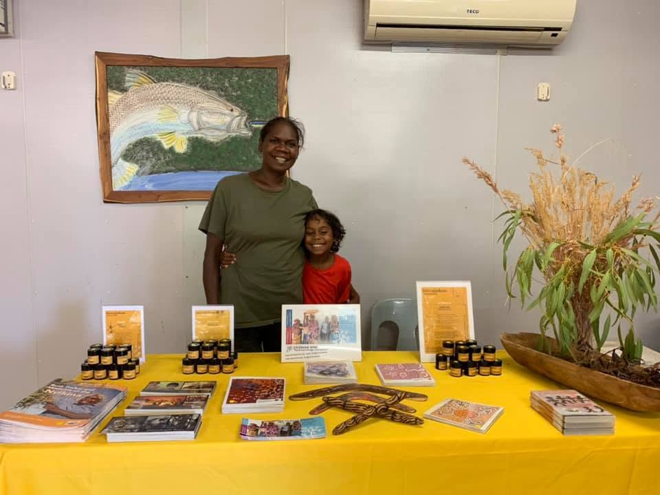 A woman and child smiling behind a table of bush products, books and artefacts