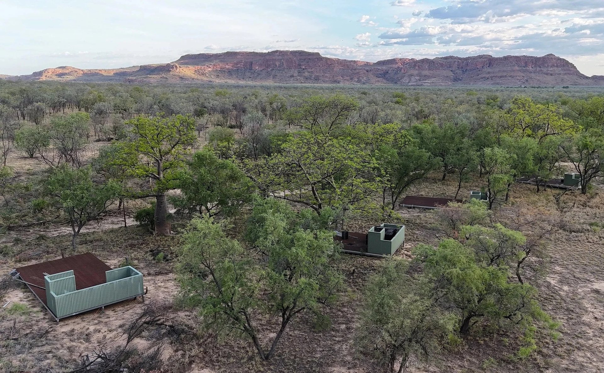 Aerial view of eco retreat accommodation platforms among trees, with a sandstone escarpment behind
