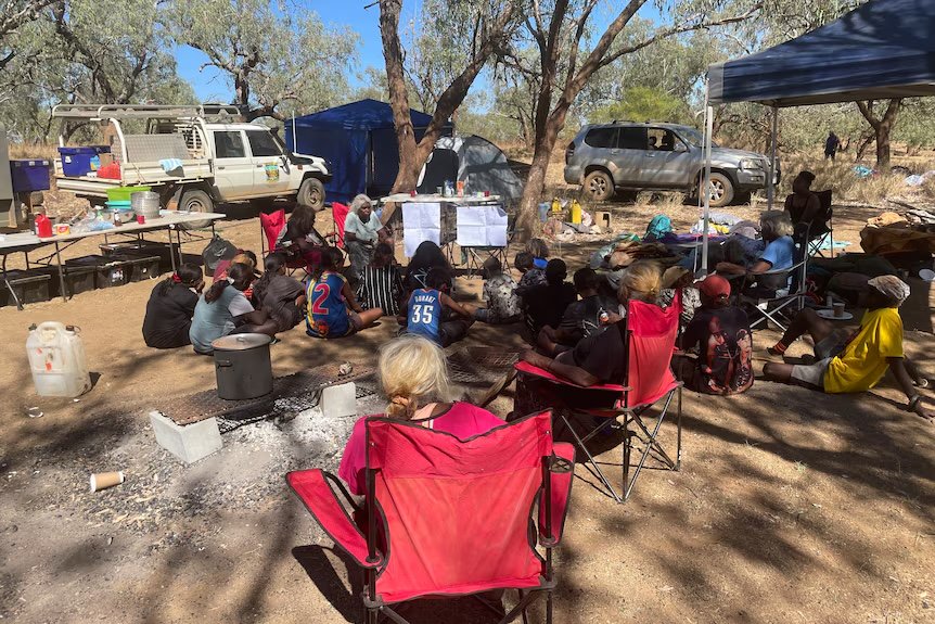 Families and young people gathered in the shade at a bush camp