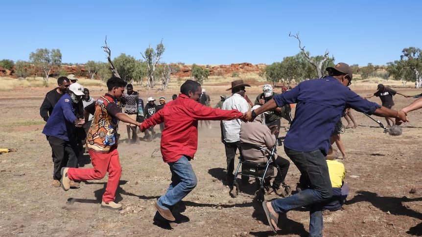 People holding hands and dancing in a circle on Country